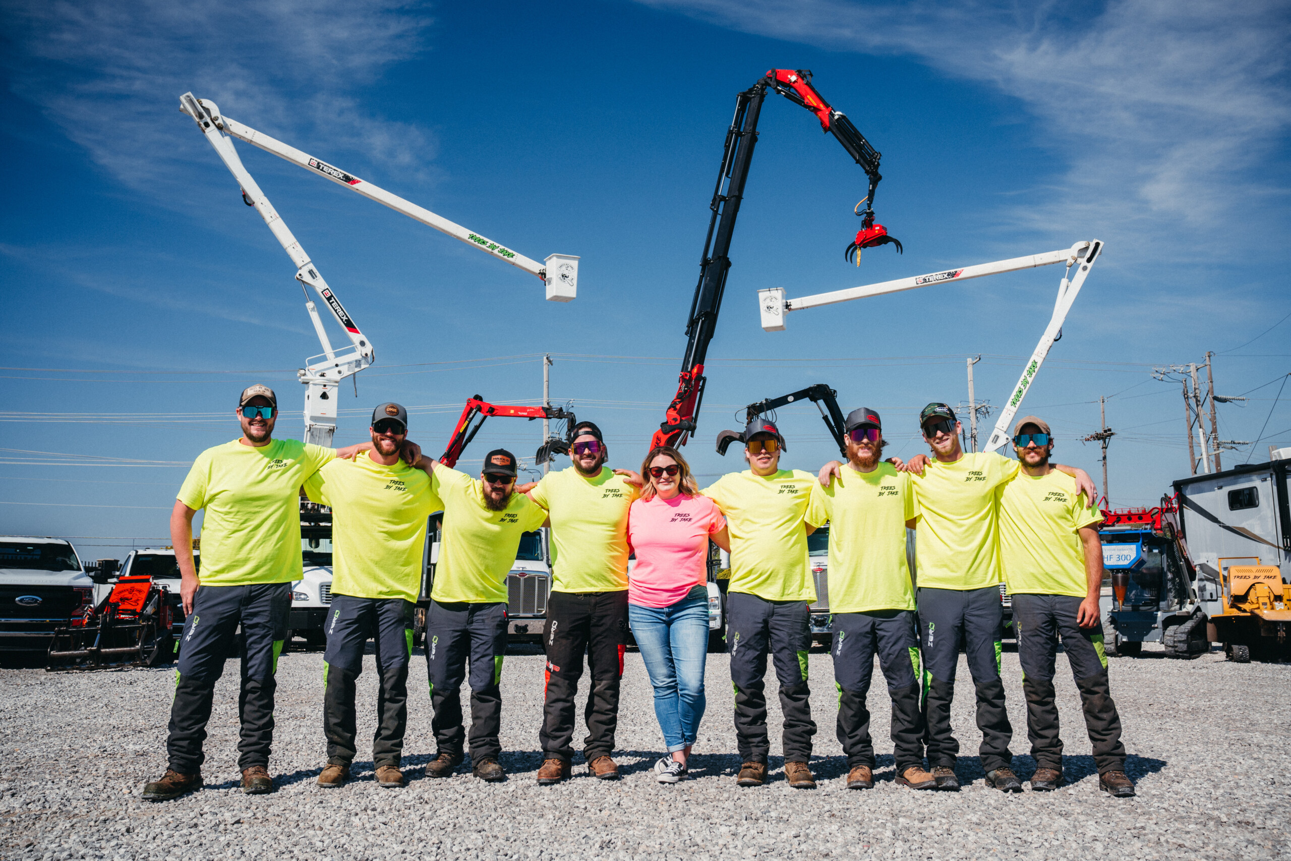 Group of workers in neon yellow shirts standing in front of large cranes in an industrial area under clear blue sky.