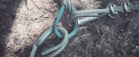 Two thick metal cables secured together with a large metal hook lying on bare, dry soil.